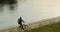 An unidentified cyclist cycles along the riverbank.