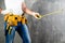 unidentified handyman standing with a tool belt with construction tools and holding roulette against grey background. DIY tools