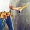 unidentified handyman standing with a tool belt with construction tools and holding roulette against grey background, toned image