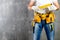 unidentified handyman standing with a tool belt with construction tools and holding a ruler against grey background. DIY tools