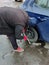 An unidentified man with a criminal appearance steals the rear wheel of a car by unscrewing it