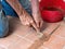 Unidentified man, workman, repairing grout between outdoor terracotta style patio tiles.