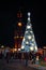 Unidentified people celebrate New Year Eve near old fire tower with clock and Chistmas tree at night, Vinnytsia, Ukraine