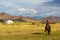 Unidentified shepherd rides horse near his yurt