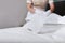 A uniformed maid adjusts the pillows on the bed. Pillows are out of focus. Unrecognizable person. Hands in white cotton gloves.