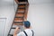 A uniformed specialist fixes a metal ladder to the hatch of the attic door