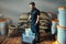 Uniformed worker weighs roasted coffee in a transparent tray on a scale in a coffee industry warehouse with bags and white buckets