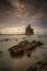 Unique rock formations on sandy Tanjung Layar Beach under dark cloudy sunset sky, long exposure