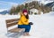 Unique Winter holidays trip to amazing snow valley - young happy and beautiful Asian woman sitting on bench alone enjoying snowy