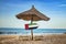 United Arab Emirates flag on wooden arrow sign. There are two sun loungers and a sun umbrella on the beach. It is a tropical