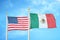 United States and Mexico two flags on flagpoles and blue cloudy sky