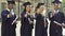 University graduates in academic regalia holding diplomas, putting thumbs-up