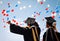 University graduates in black robes rejoice, raise their hands up against the sky and balloons