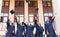 University graduates  throwing graduation hats in the air. Group of happy graduates in academic dresses near university building