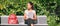 University student sitting on park bench on campus holding laptop. Panoramic of Asian young woman with backpack, books