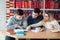 University students sitting together at table with books and laptop. Happy young people doing group study in library