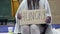 An unkempt-looking young woman sits with a begging cup and holds a handwritten HUNGRY poster.