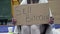 An unkempt-looking young woman sits with a begging cup and holds a handwritten SELL BITCOIN poster.