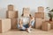 Unknown anonymous woman wearing white t shirt sitting on floor surrounded with cardboard boxes with belongings, having carton box