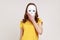 Unknown anonymous woman in yellow casual style t-shirt covering her face with white mask, hiding