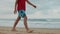 Unknown boy enjoying summer at beach. Unrecognizable guy walking along seaside.