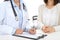 Unknown doctor and female patient discussing something while standing near reception desk in emergency hospit