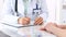 Unknown doctor woman consulting patient while filling up an application form at the desk in hospital. Just hands close