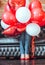 Unknown girl hidden in red and white helium balloons on sofa. Colorful balloons and women legs in red shoes. Birthday decoration.