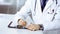 Unknown male doctor sitting and working with clipboard of medication history record in clinic at his working place