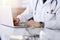 Unknown male doctor sitting and working with laptop in a darkened clinic, glare of light on the background, close-upof