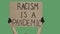 An unknown person is holding a poster from a cardboard box with the words RACISM IS A PANDEMIC with both hands. Equality