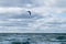 Unknown person in special black suit engaged in kitesurfing moves to right behind  kite in distance on horizon of stormy sea