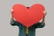 Unknown unrecognizable woman hiding her face behind big red heart, hesitates to confess his feelings