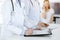 Unknown woman-doctors at work with patient at the background. Female physicians filling up medical documents or