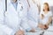 Unknown woman-doctors at work with patient at the background. Female physicians filling up medical documents or