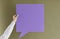 Unknown woman holding blank purple paper card in form of speech bubble on green khaki background.