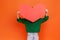 Unknown woman wearing green casual style sweater holding big red paper heart, hiding behind love