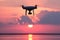 Unmanned aerial vehicle on a background of pink clouds. Silhouette of radio-controlled drone over the water surface at sunset. The