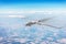Unmanned military aircraft flies high in the sky at high speed over fields, blue sky clouds