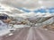 Unpaved mountain road in the winter with snow and cloudy sky