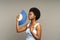 Unpleased afro woman suffer from heat inside, overheated african female waving with paper fan