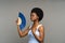 Unpleased afro woman suffer from heat inside, overheated african female waving with paper fan