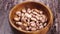 Unprocessed pinto beans falling into a wooden bowl on a rustic wood surface in slow motion.