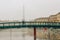 Unrecognisable couple standing on Alexander Langer bridge, Darsena waterfront on foggy winter morning, Milano city