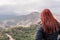 unrecognisable red-haired woman watches from above mountains on a cloudy day