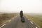 Unrecognisable woman, walking with suitcase in hand on a cold and foggy mountain road