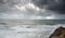 Unrecognised person standing the edge of a cliff end enjoying the dramatic stormy sea and sky