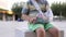 Unrecognizable 2 years old boy with broken hand in bandage is sitting outdoors in city park on summer day. Child with a
