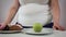 Unrecognizable adult Caucasian woman standing at the table with sweets and apple on it. Obese girl selecting between