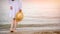 Unrecognizable alone woman with straw hat in hand on seashore. Silhouette of woman from back with thin legs in white beach dress